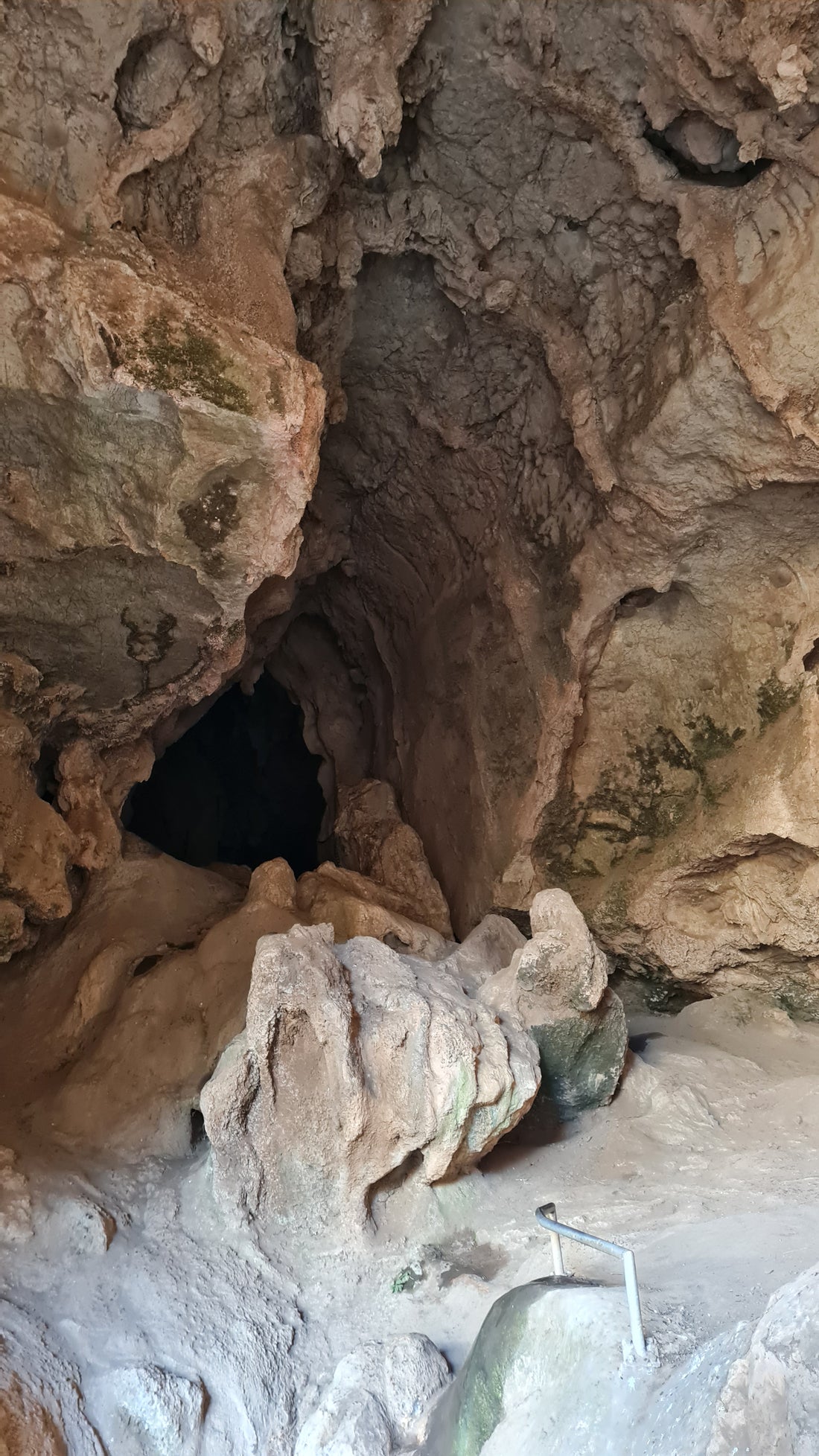 An image of a cave featuring sculpted rock and a dark hole. In the foreground is a railing to assist walkers